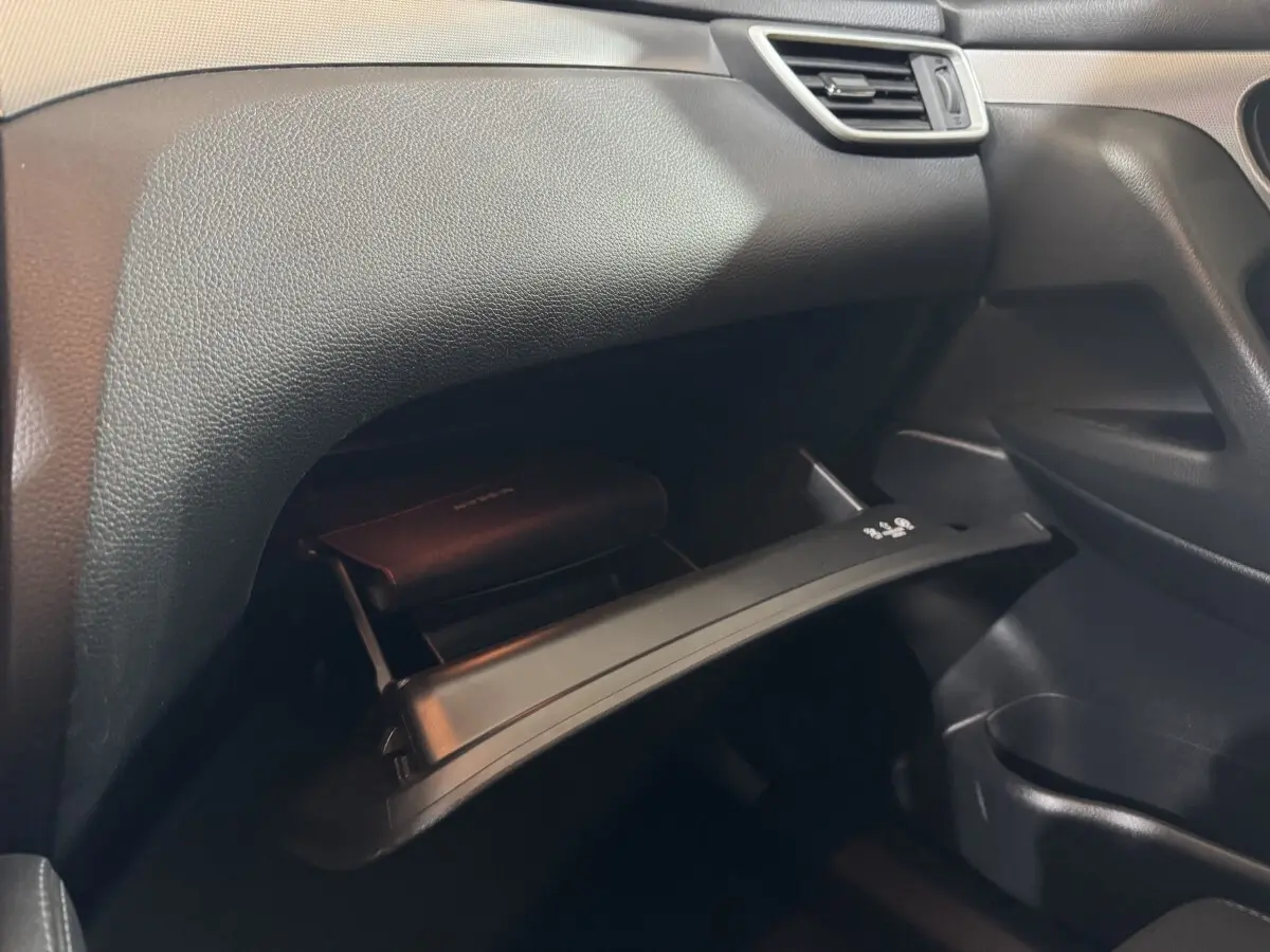 Vue intérieure du côté passager du Nissan Qashqai 2019, boîte à gants ouverte avec manuel visible, tableau de bord noir.