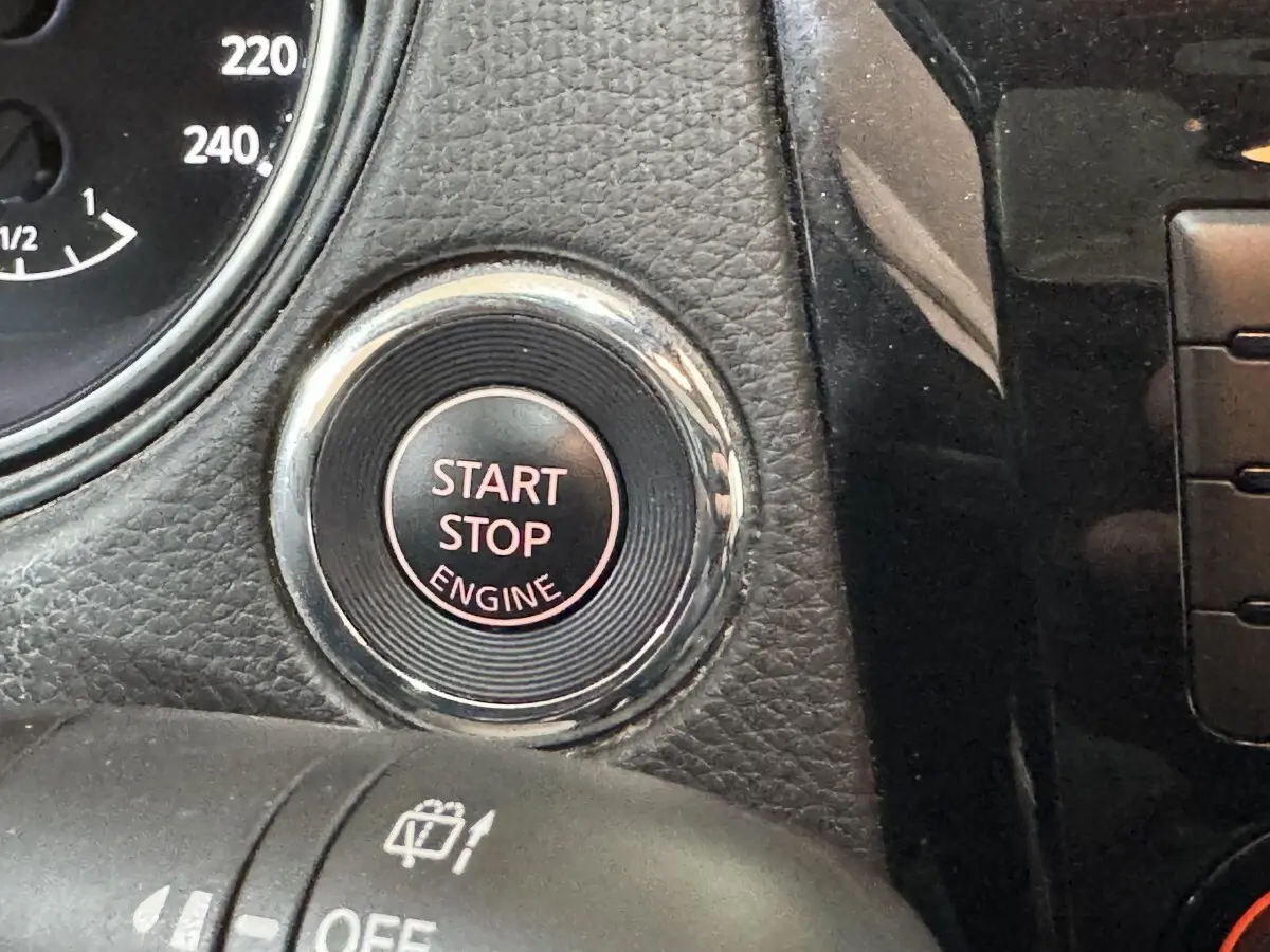 Gros plan sur le bouton Start Stop Engine entouré de chrome dans l’habitacle noir du Nissan Qashqai gris foncé.
