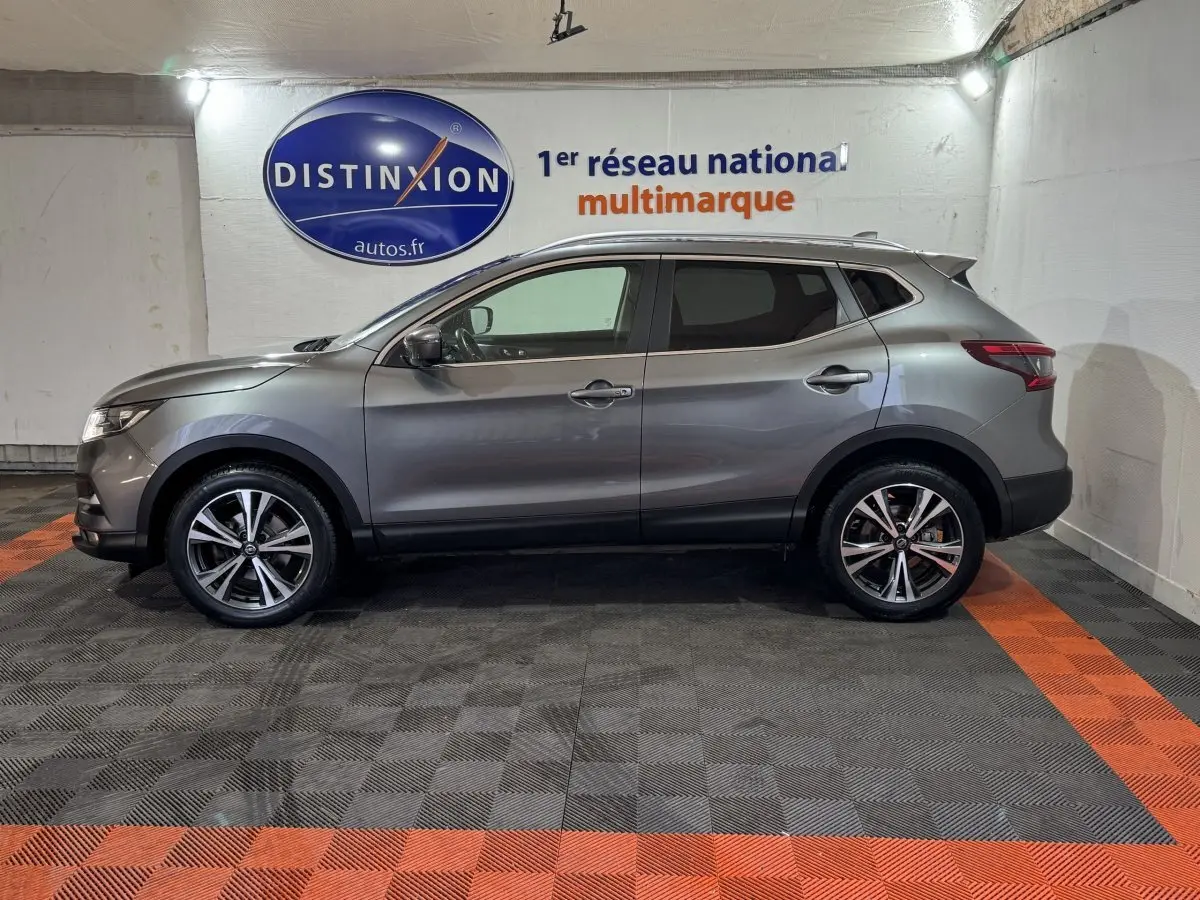 Profil droit d'un Nissan Qashqai gris foncé 2019, avec jantes alliage et vitres teintées, en intérieur showroom.