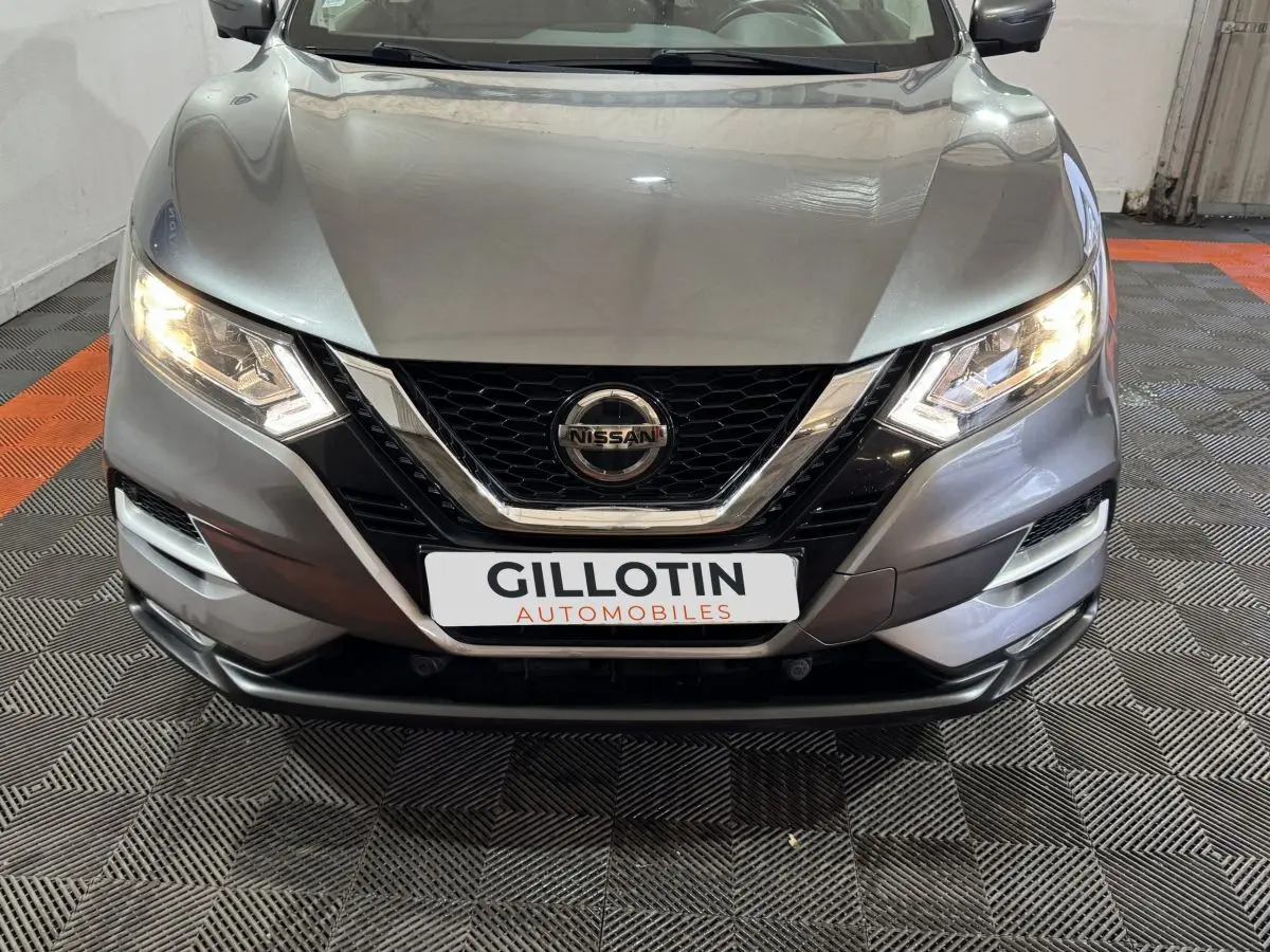 Vue avant du Nissan Qashqai gris foncé 2019 avec phares allumés et calandre chromée distinctive.