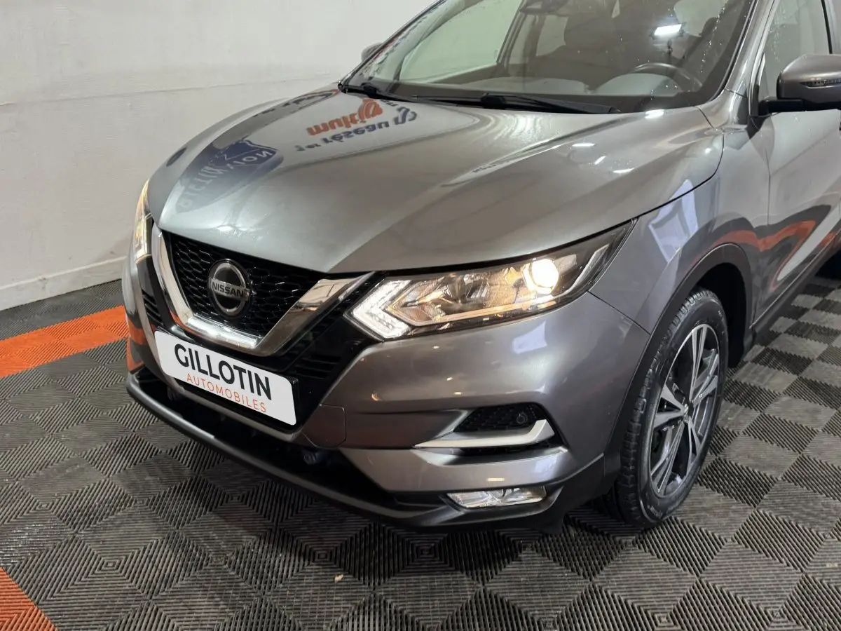 Vue 3/4 avant droit du Nissan Qashqai gris foncé avec phares allumés et calandre chromée distinctive.