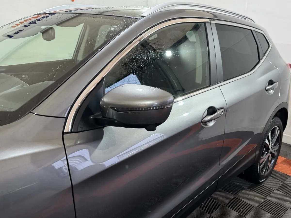 Vue côté gauche avant d'un Nissan Qashqai gris foncé 2019 avec rétroviseur et jante alliage visibles.