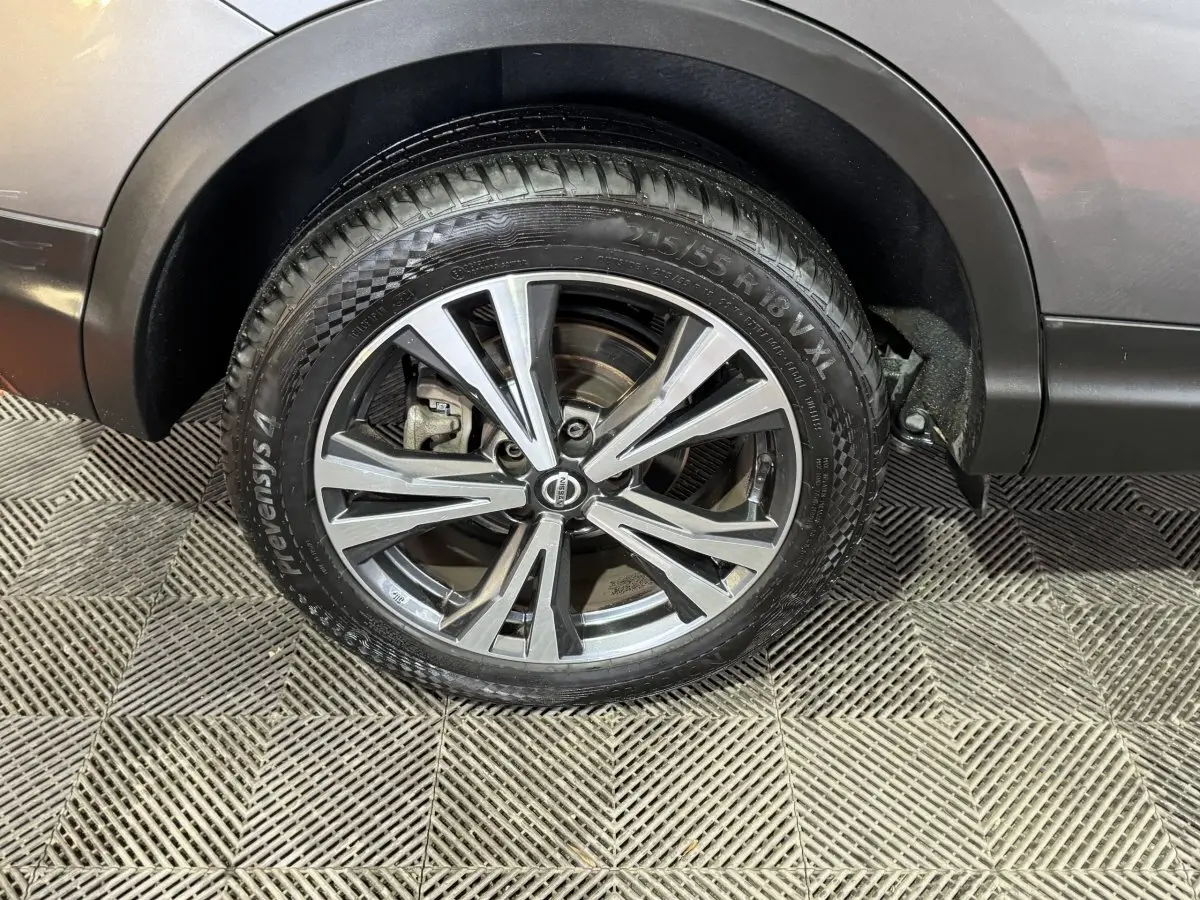 Gros plan sur la roue avant droite du Nissan Qashqai gris foncé, mettant en valeur la jante alu et cuir.