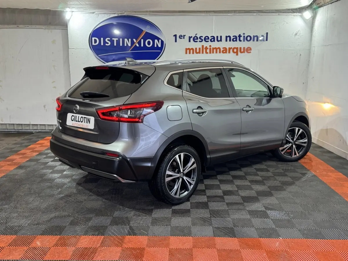 Vue 3/4 arrière droite d'un Nissan Qashqai gris foncé avec jantes alliage et feux arrière LED, en intérieur showroom.
