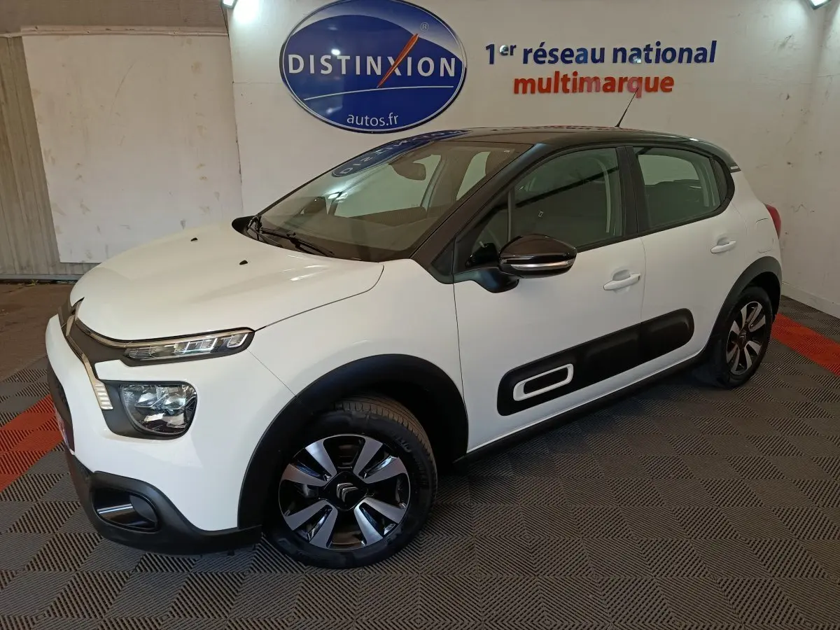 Citroën C3 blanche vue 3/4 avant droit, avec protections latérales noires et jantes bicolores.