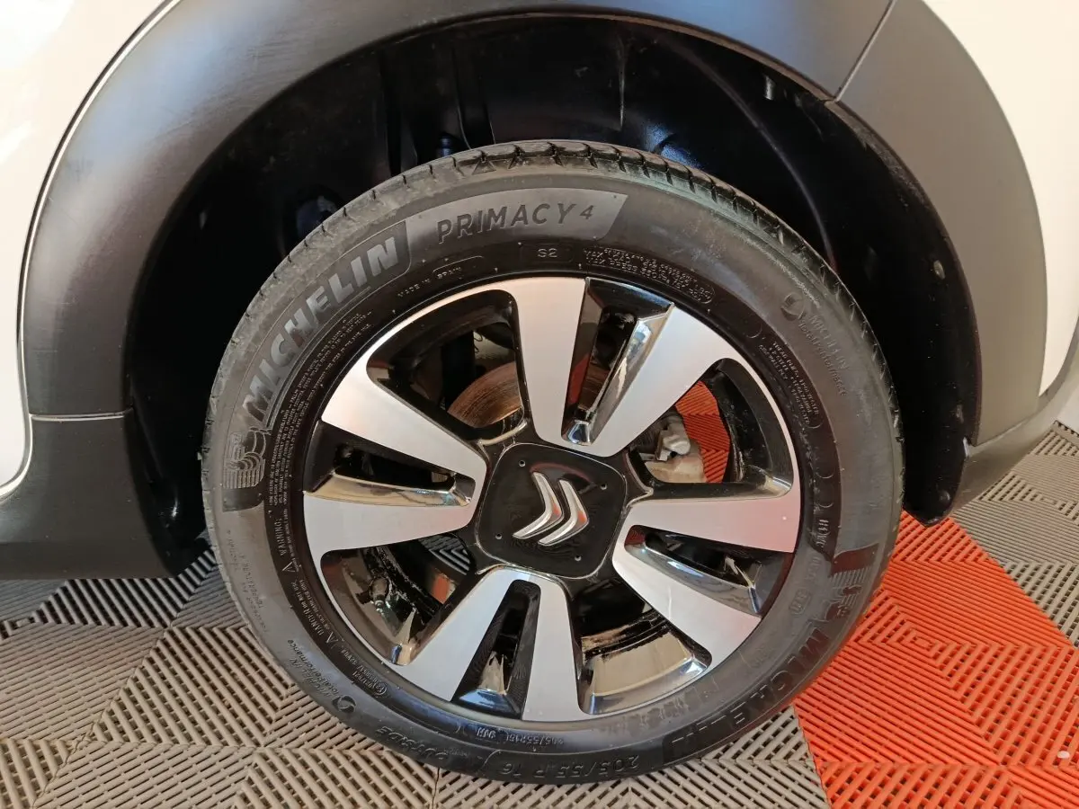 Gros plan sur la roue avant droite d'une Citroën C3 blanche, jante alliage bicolore avec logo Citroën au centre.