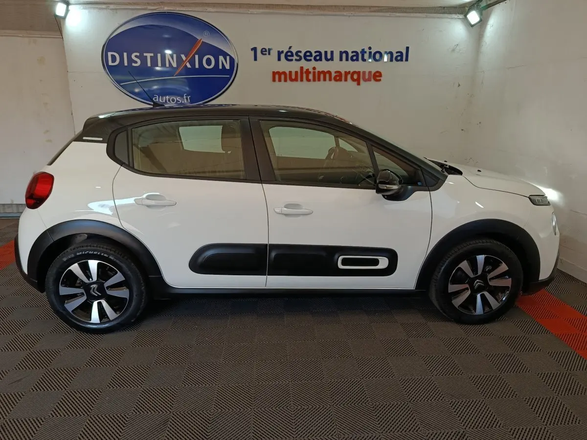 Profil droit d'une Citroën C3 blanche 2021 avec protections latérales noires et jantes bicolores en intérieur showroom.