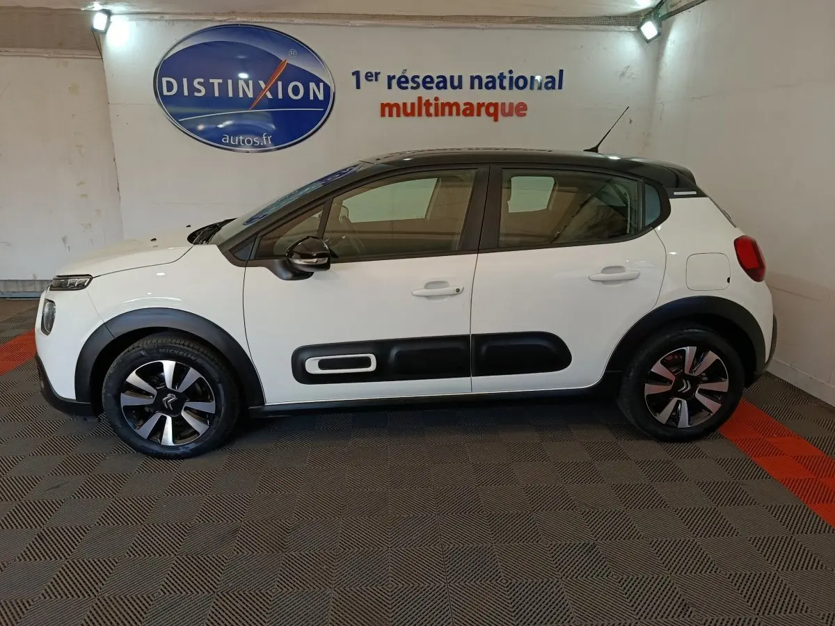 Profil côté gauche d'une Citroën C3 blanche 2021 avec protections noires et jantes bicolores en intérieur showroom.