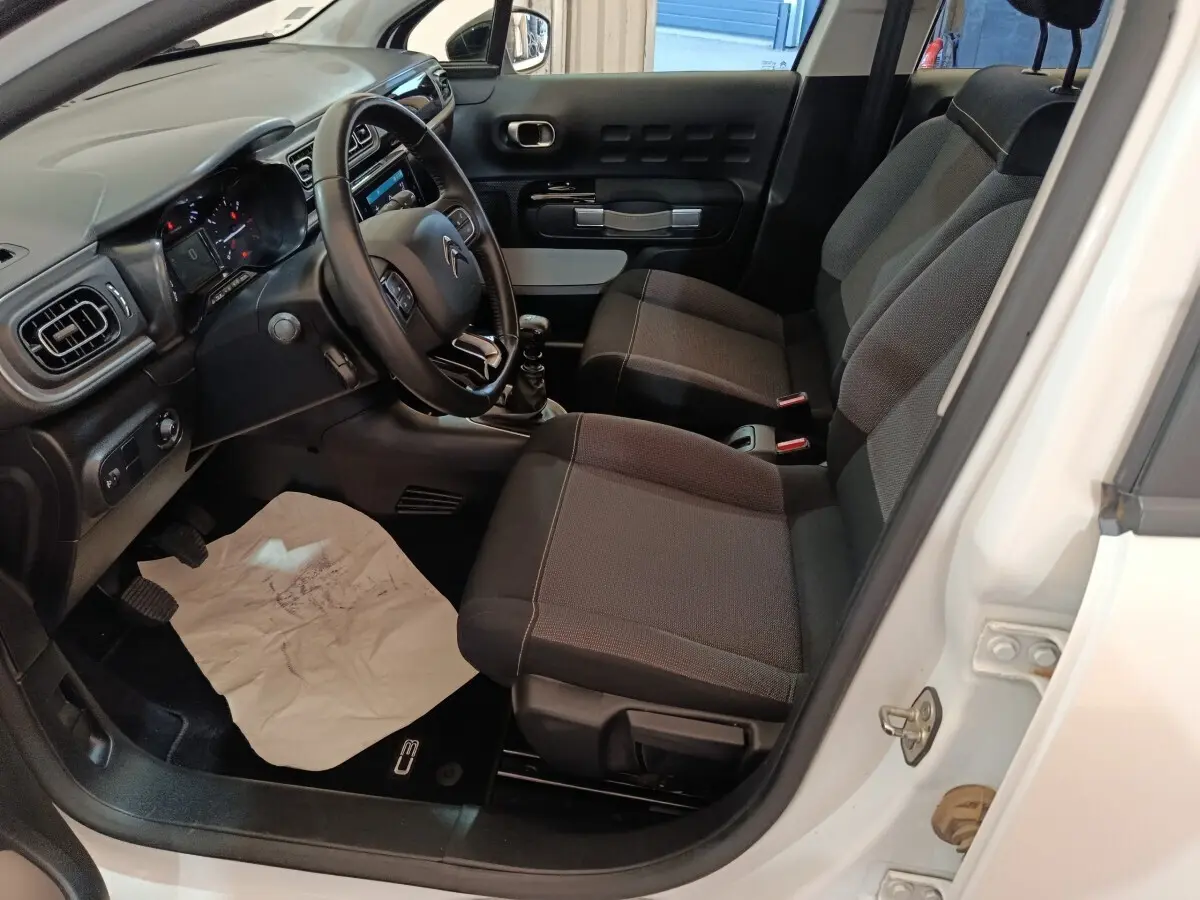 Vue intérieure côté conducteur d'une Citroën C3 blanche 2021 avec sièges tissu noirs et volant cuir multifonctions.