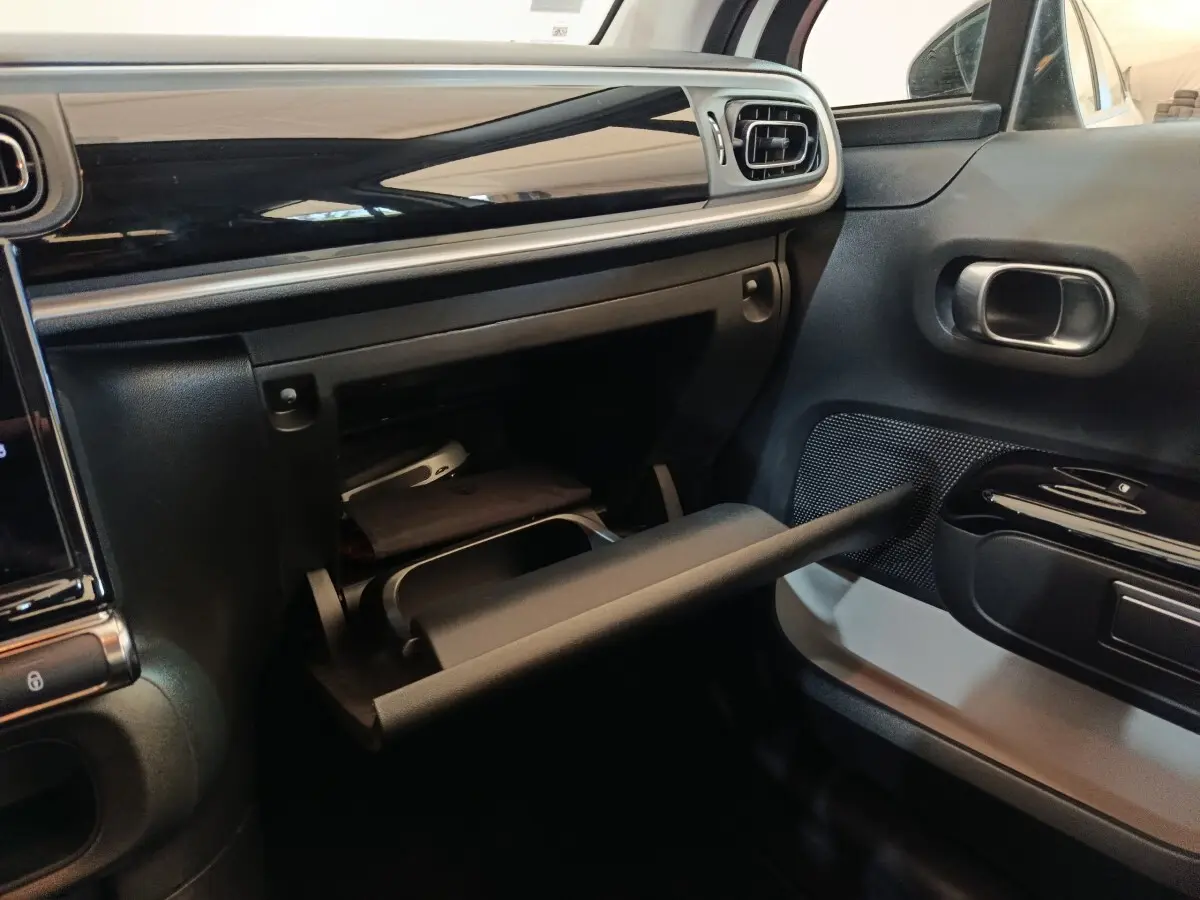 Intérieur de la Citroën C3 2021 blanc, vue côté passager sur la boîte à gants ouverte et tableau de bord noir brillant.