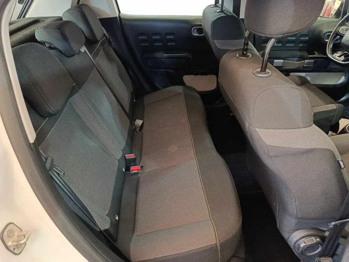 Vue intérieure côté gauche montrant la banquette arrière noire et les sièges avant d'une Citroën C3 blanche.
