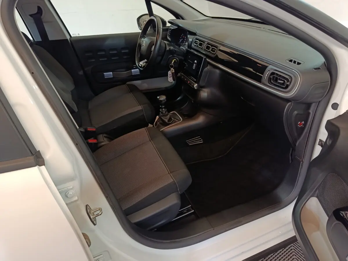 Intérieur avant droit d'une Citroën C3 blanche 2021, montrant sièges tissu, volant cuir et tableau de bord noir brillant.