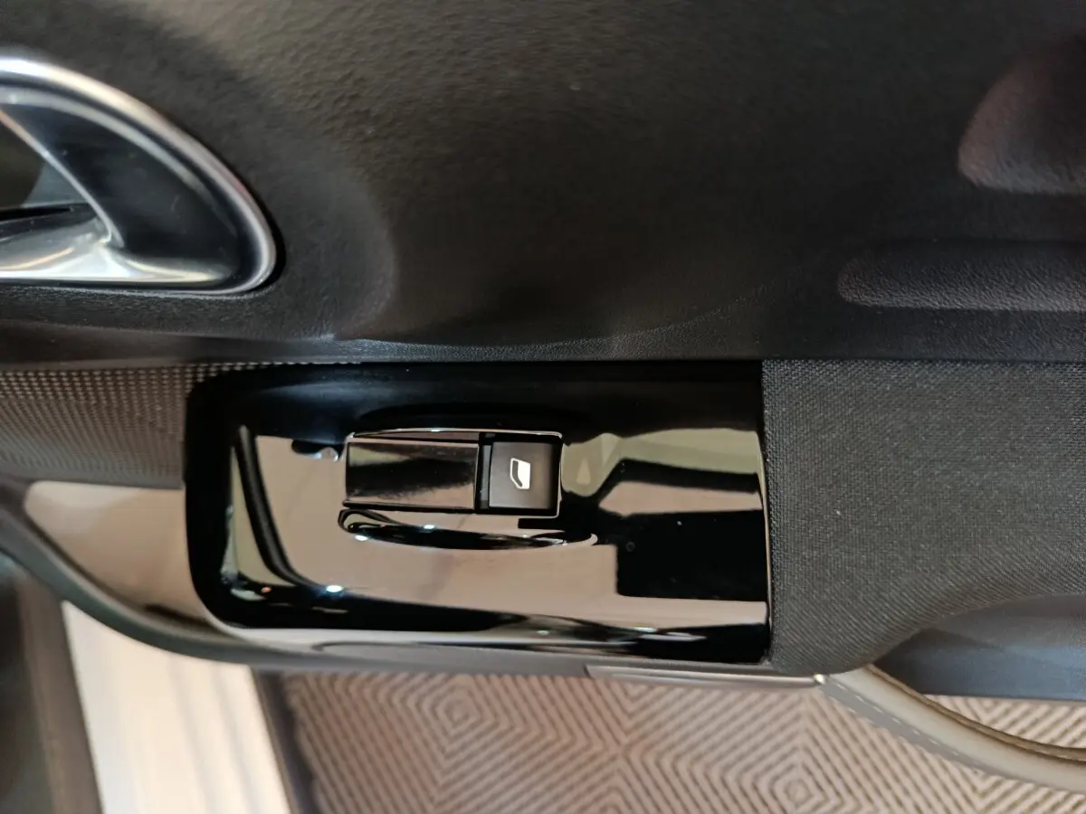 Gros plan sur le bouton de commande de la vitre électrique côté conducteur d'une Citroën C3 blanche.