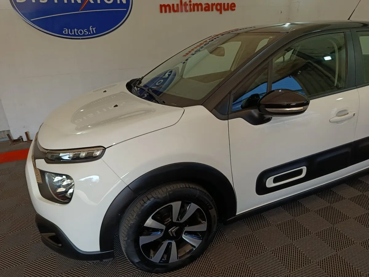 Vue 3/4 avant droit d'une Citroën C3 blanche avec protections latérales noires et jantes bicolores.