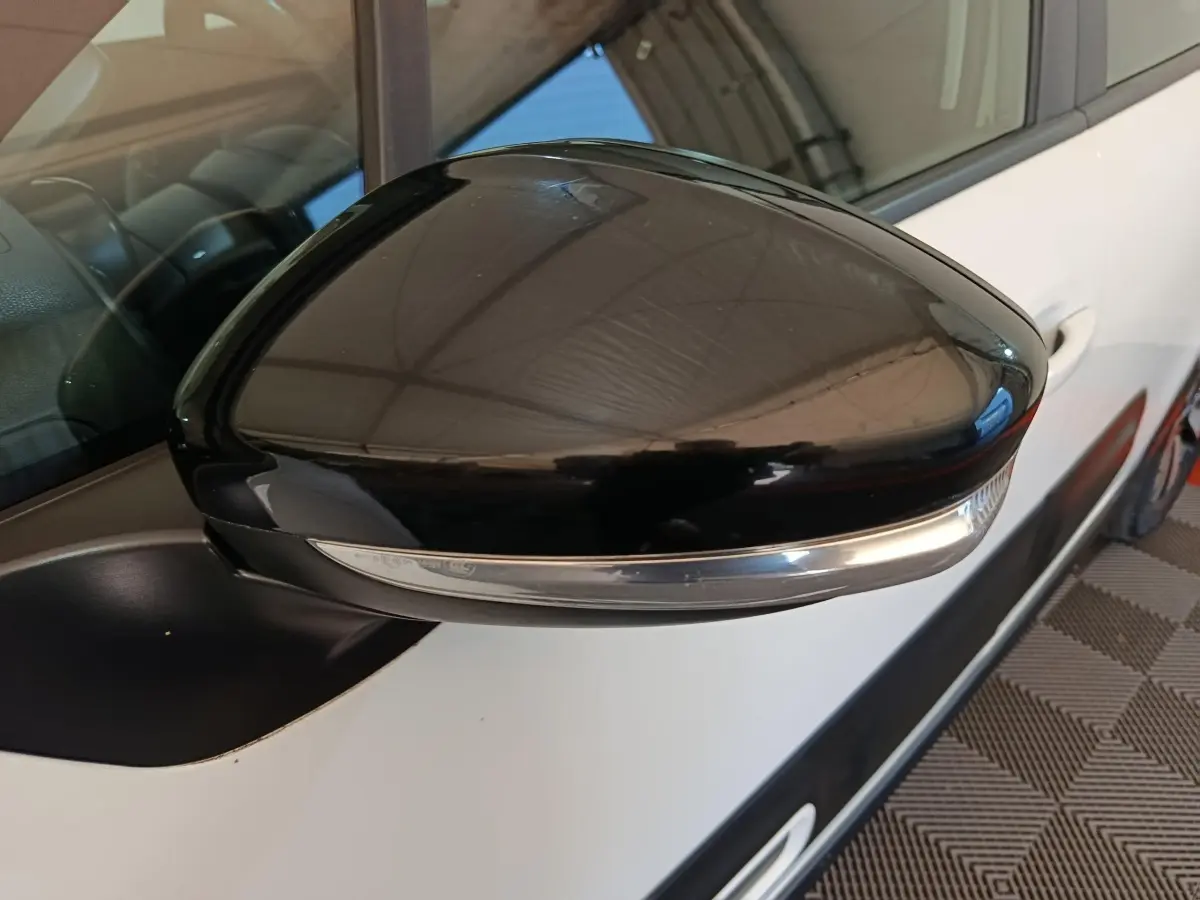 Gros plan sur le rétroviseur noir côté gauche d'une Citroën C3 blanche, avec clignotant intégré.