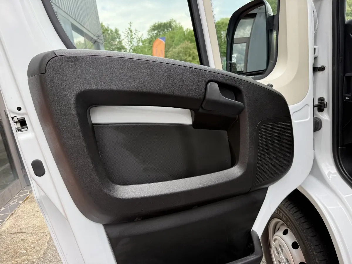 Vue rapprochée de la porte avant gauche blanche du Peugeot Boxer Fourgon 2023 avec poignée noire et haut-parleur intégré.