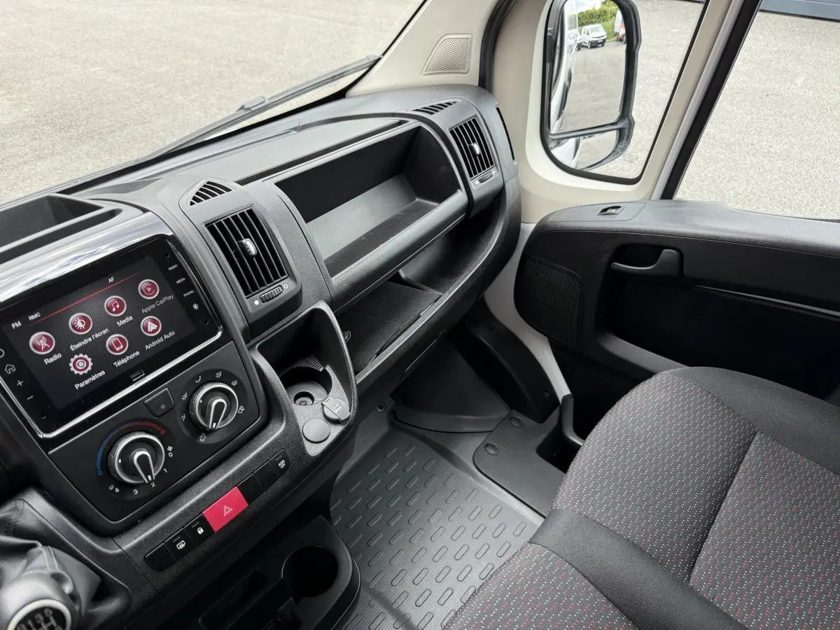 Vue intérieure côté passager du Peugeot Boxer Fourgon blanc 2023, montrant tableau de bord et siège tissu gris à motifs rouges.