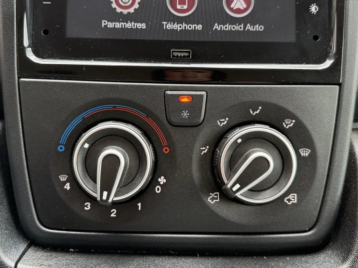 Gros plan sur les commandes de climatisation du Peugeot Boxer Fourgon blanc, avec boutons rotatifs et écran tactile partiel visible.