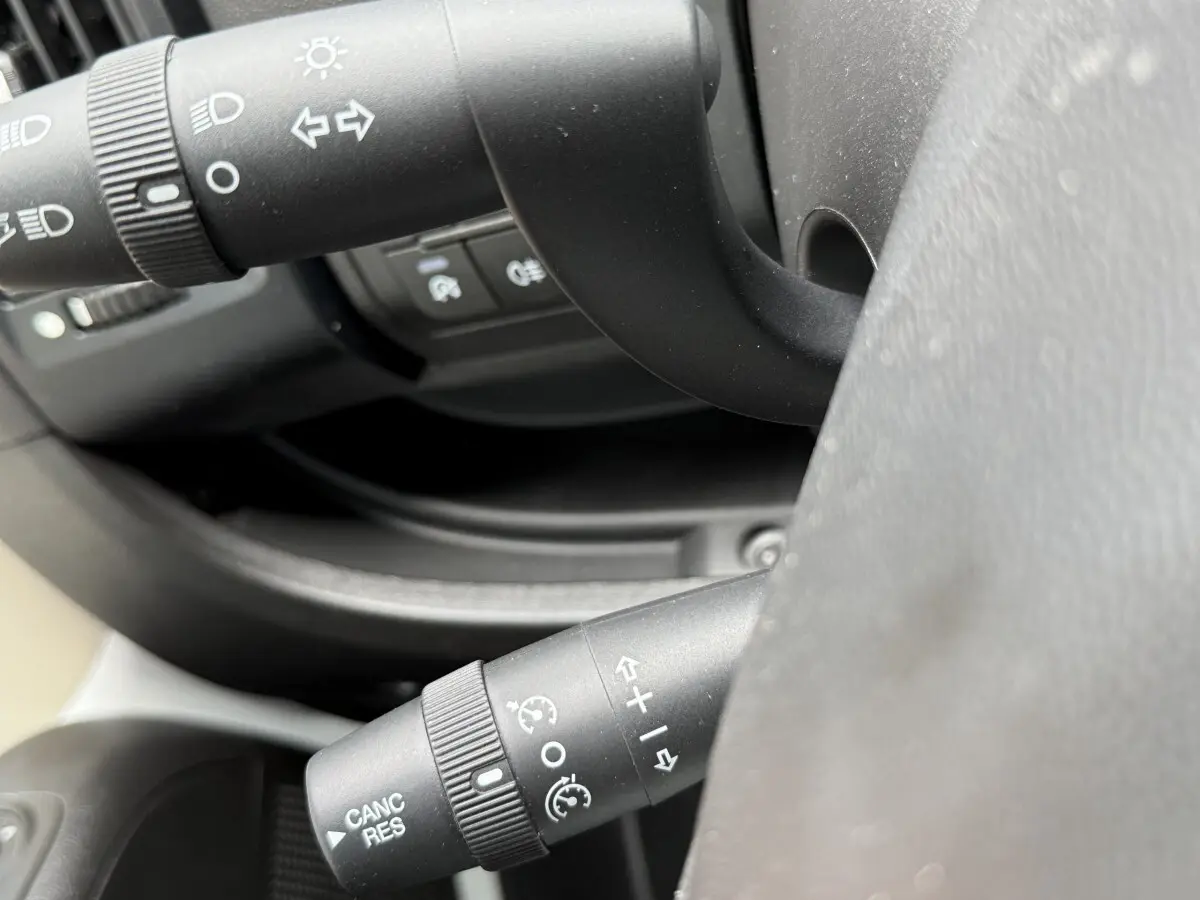 Gros plan sur les commandes de volant multifonctions noir du Peugeot Boxer Fourgon blanc, côté gauche du poste de conduite.
