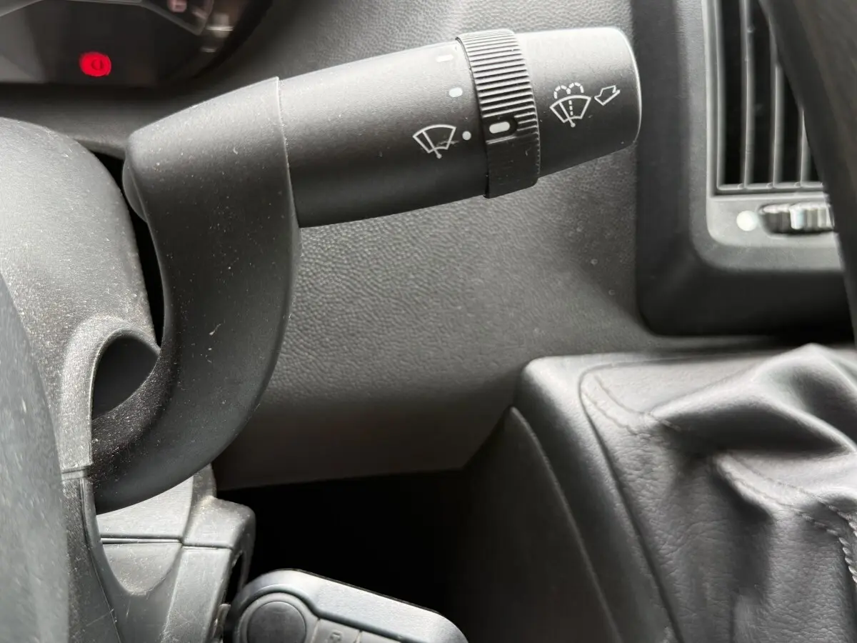 Gros plan sur la manette d’essuie-glace et le levier de vitesse en cuir noir dans l’habitacle du Peugeot Boxer Fourgon blanc.