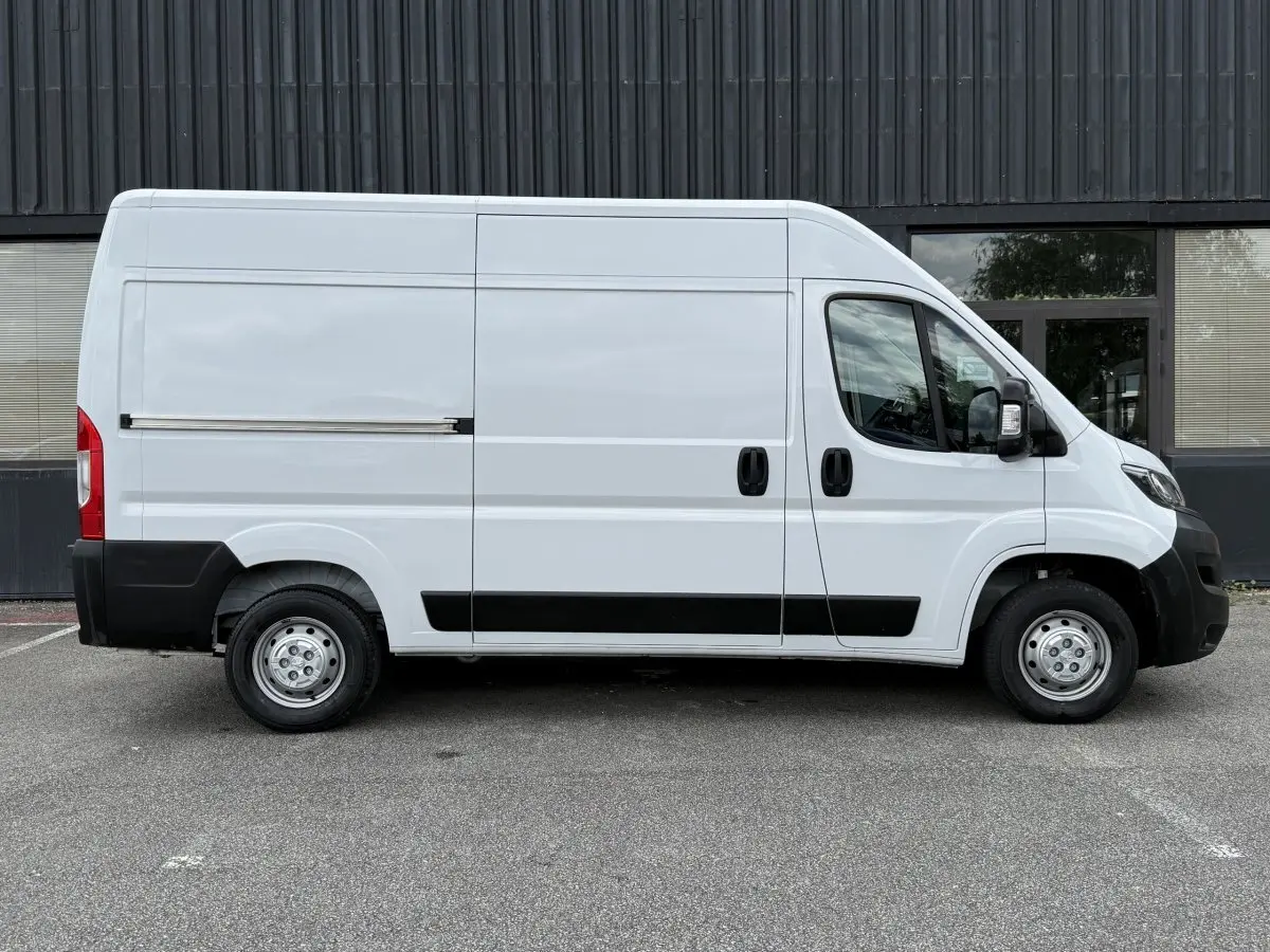 Vue de profil côté droit d’un Peugeot Boxer Fourgon blanc avec protections noires sur les bas de caisse et pare-chocs.