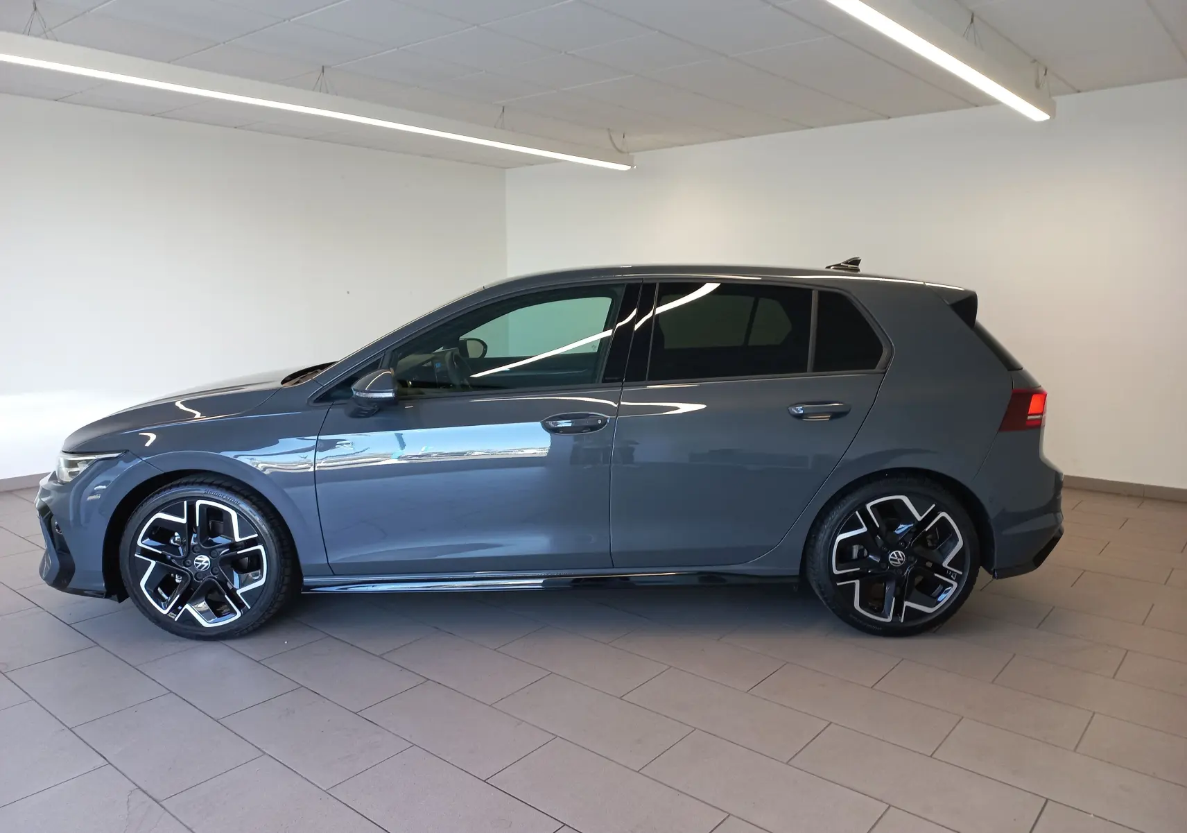 Profil gauche d'une Volkswagen Golf 1.5 eTSI 150 DSG7 R-Line Edition gris dauphin avec jantes noires et détails sportifs.