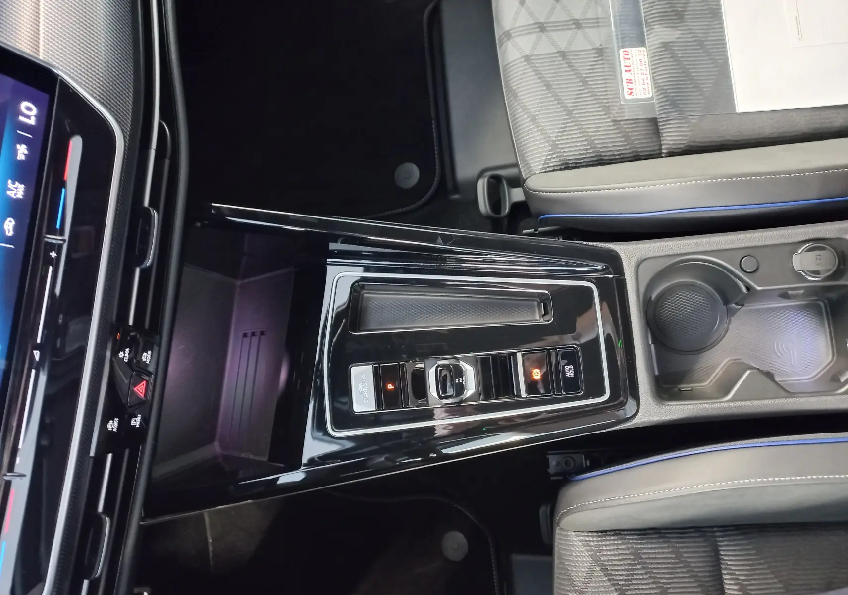 Vue rapprochée de la console centrale noire brillante de la Volkswagen Golf 1.5 eTSI 150 DSG7 R-Line Edition, sièges gris à surpiqûres bleues.