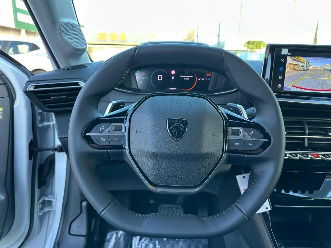 Vue intérieure centrée sur le volant cuir noir de la Peugeot 208 Hybrid 110 blanc avec cockpit numérique et écran tactile.