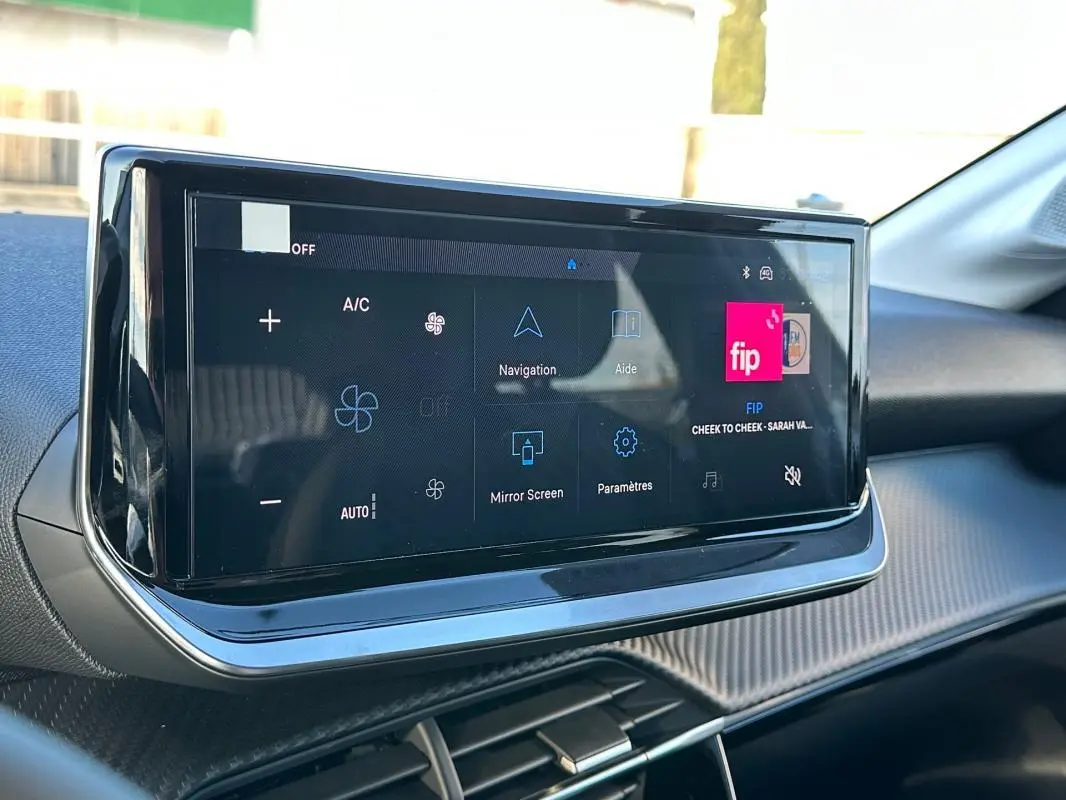 Écran tactile du tableau de bord de la Peugeot 208 Hybrid 110 blanc, vue rapprochée côté passager.