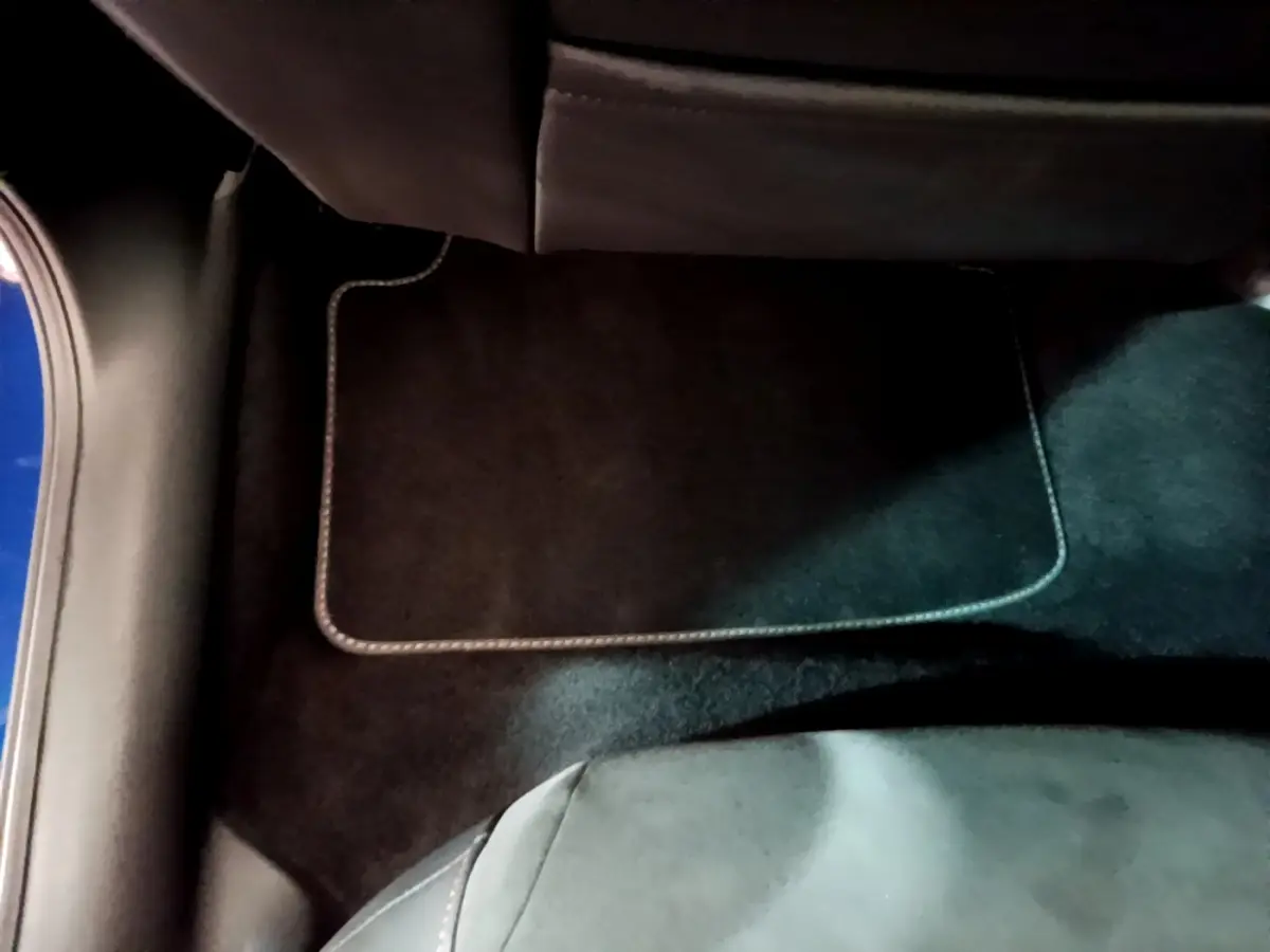 Vue intérieure du plancher côté passager arrière d'un SEAT Leon bleu, avec tapis de sol noir et couture claire visible.