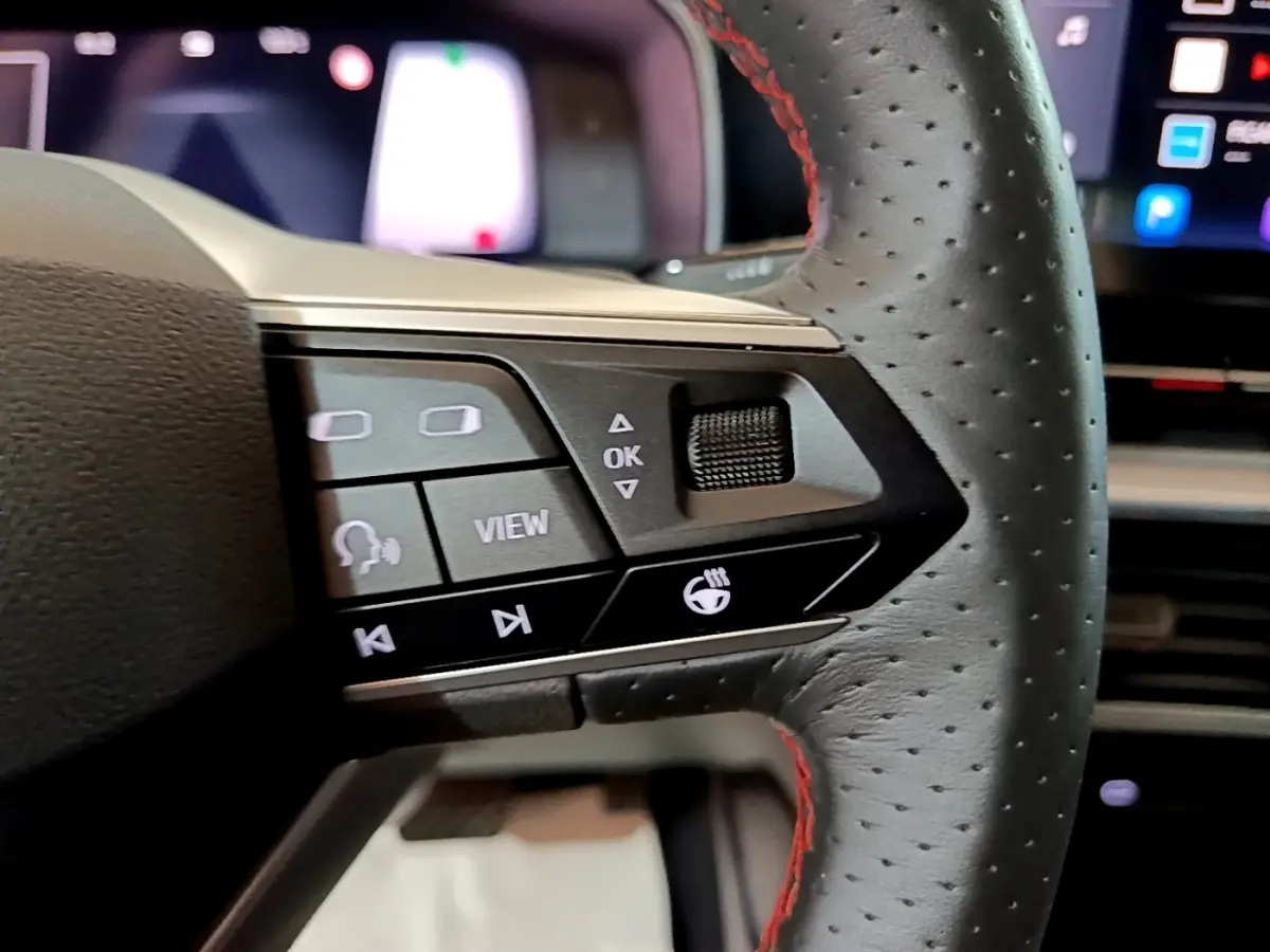 Gros plan sur les commandes gauche du volant en cuir noir perforé avec surpiqûres rouges du SEAT Leon bleu 2021.