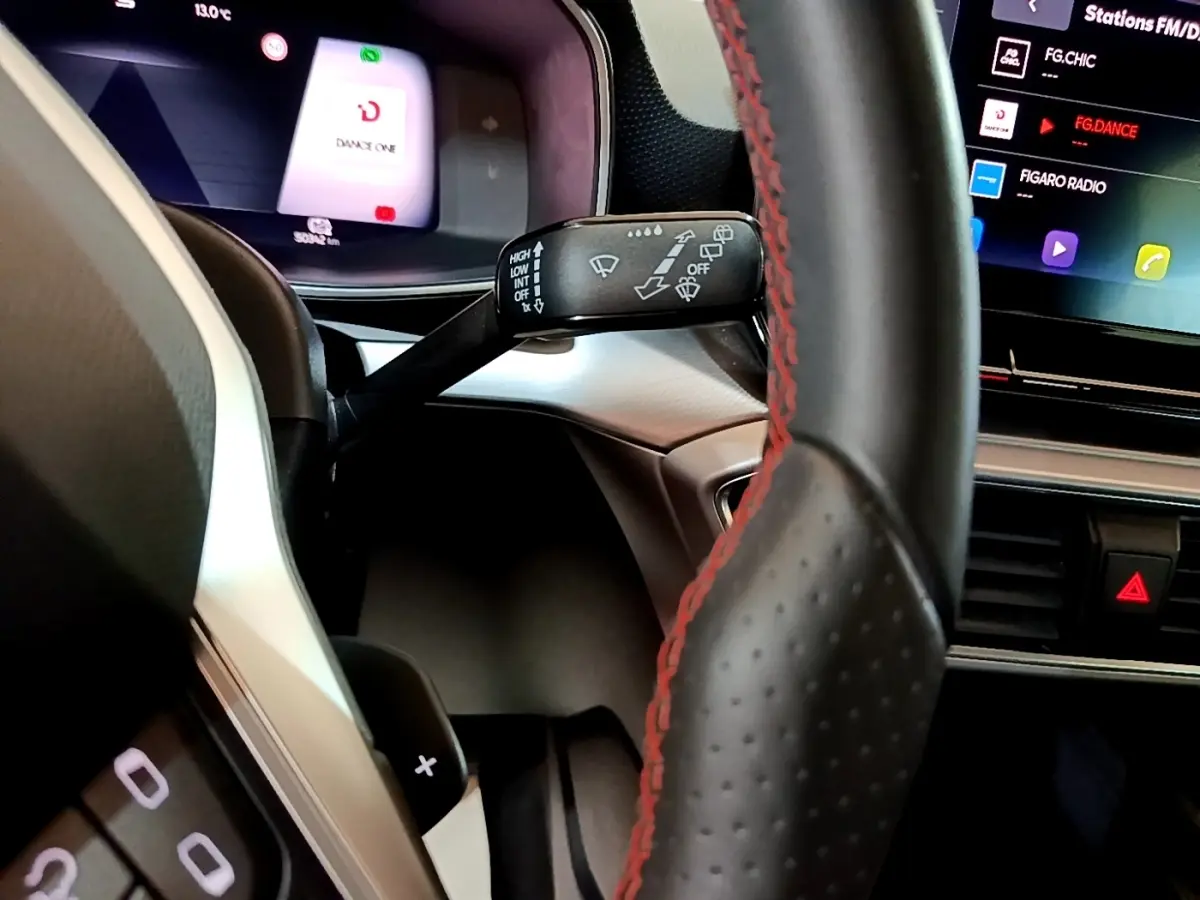 Gros plan intérieur sur le volant cuir noir avec surpiqûres rouges et le combiné d'instruments digital du SEAT Leon 2021.