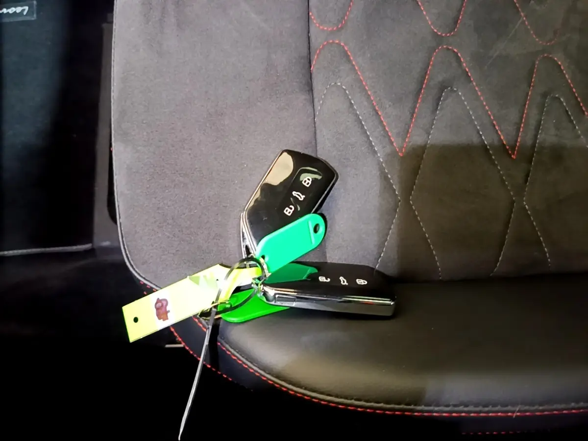 Gros plan sur les clés de voiture SEAT Leon posées sur un siège tissu noir avec surpiqûres rouges.