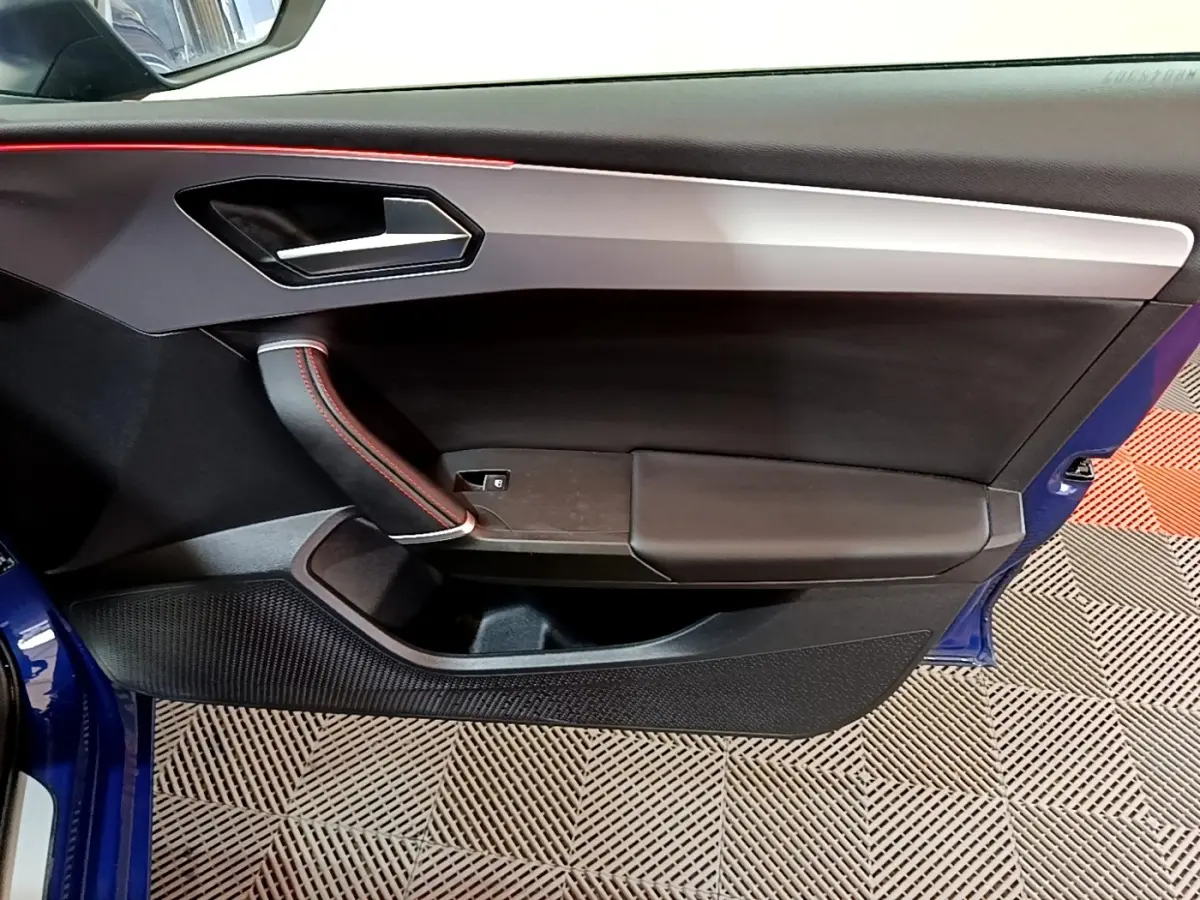 Vue intérieure côté gauche de la porte avant bleu avec surpiqûres rouges et poignée intégrée du SEAT LEON 1.5 eTSI 2021.