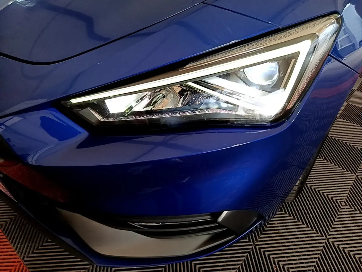 Gros plan sur le phare avant droit allumé d’une SEAT LEON bleu électrique, soulignant ses lignes anguleuses modernes.