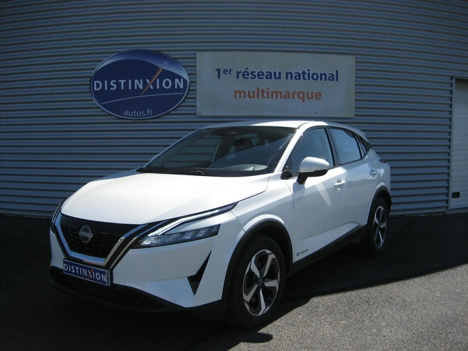Nissan Qashqai blanc nacré en 3/4 avant droit, avec calandre noire et jantes bicolores distinctives.