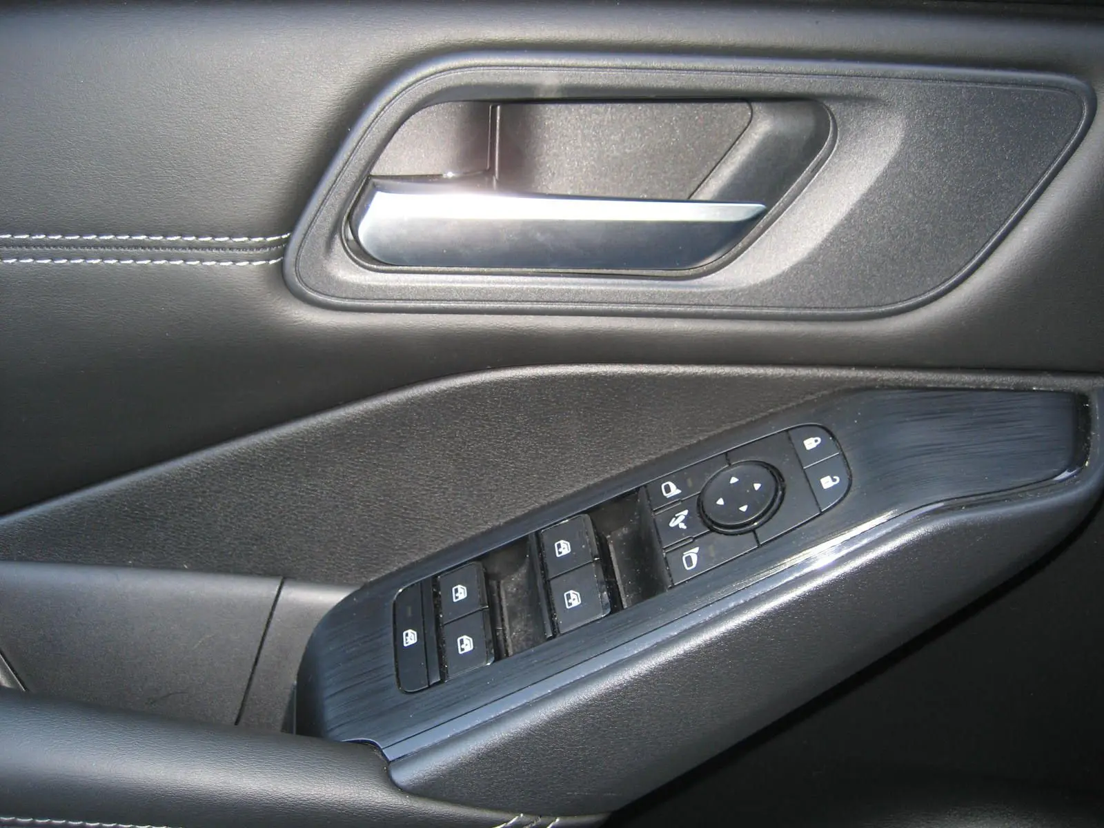 Gros plan sur la commande de lève-vitres et la poignée intérieure côté conducteur du Nissan Qashqai blanc nacré 2024.