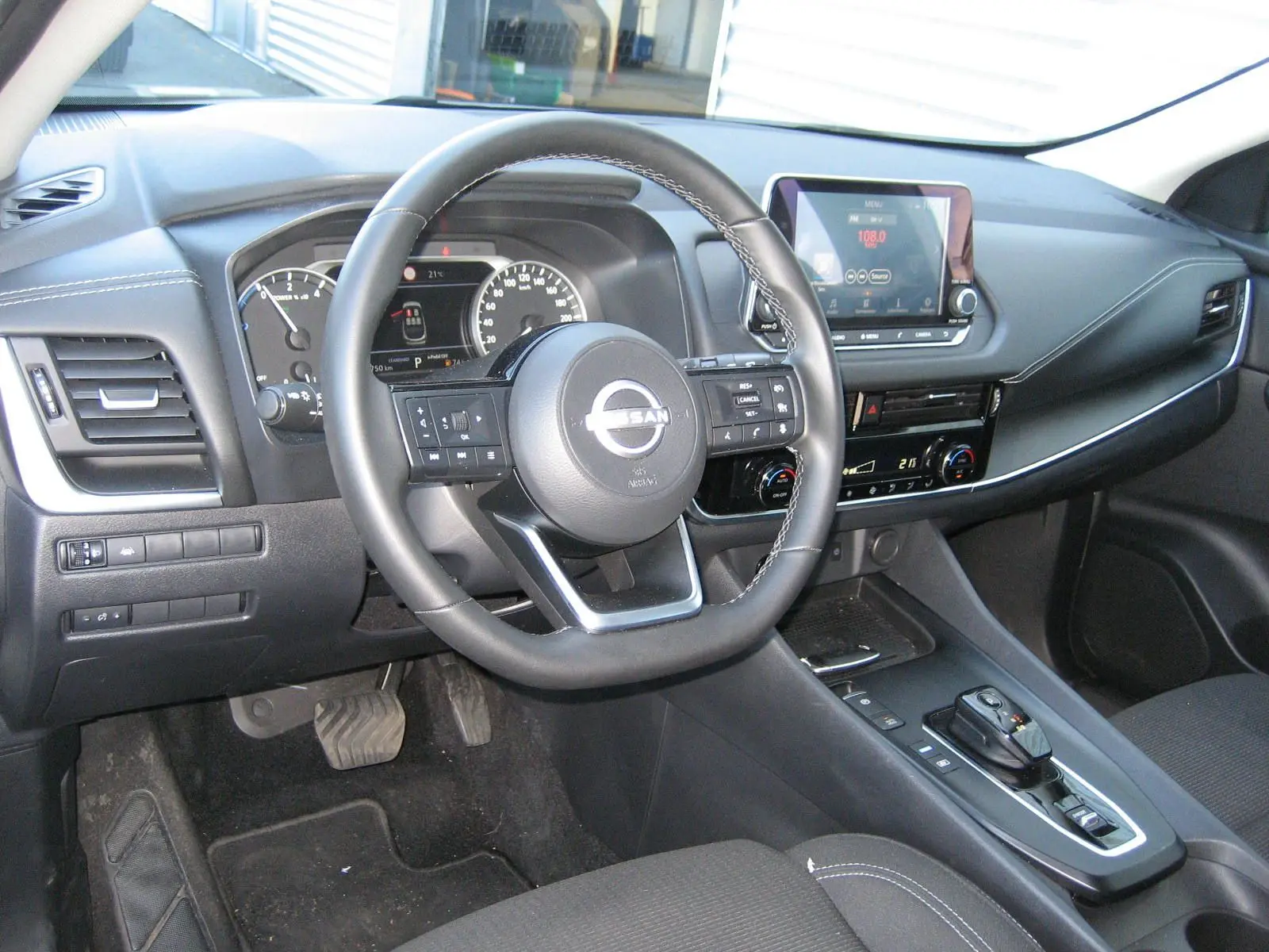 Vue intérieure côté conducteur du Nissan Qashqai 2024, tableau de bord noir avec écran tactile et volant multifonction.