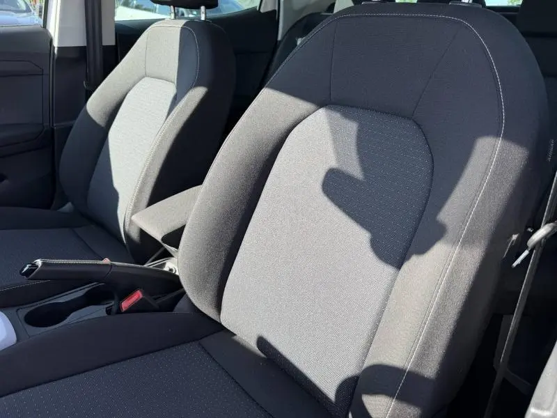 Gros plan sur les sièges avant gris tissu Como du SEAT Arona 2025, avec accoudoir central et frein à main en cuir visible.