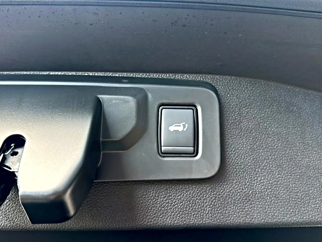 Gros plan sur le bouton d'ouverture électrique du hayon dans le coffre du Renault Austral bleu outremer 2026.