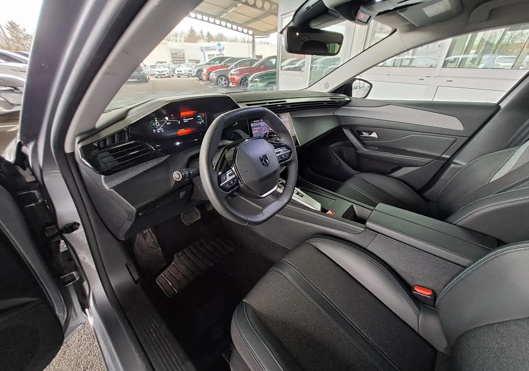 Intérieur de la Peugeot 308 gris Artense 2023, vue côté conducteur, tableau de bord numérique et sièges noirs modernes.