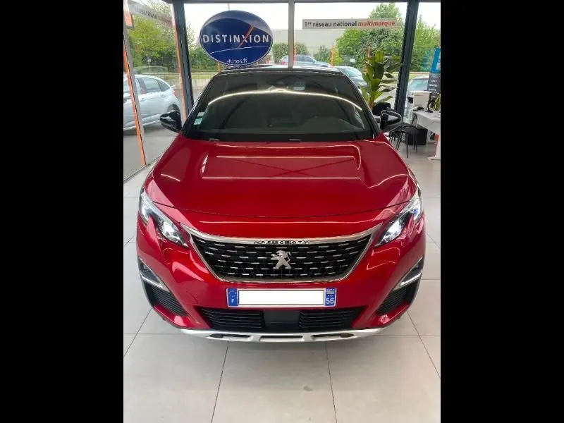 Vue frontale d'un Peugeot 3008 rouge vif exposé en showroom, soulignant sa calandre chromée et ses phares LED modernes.
