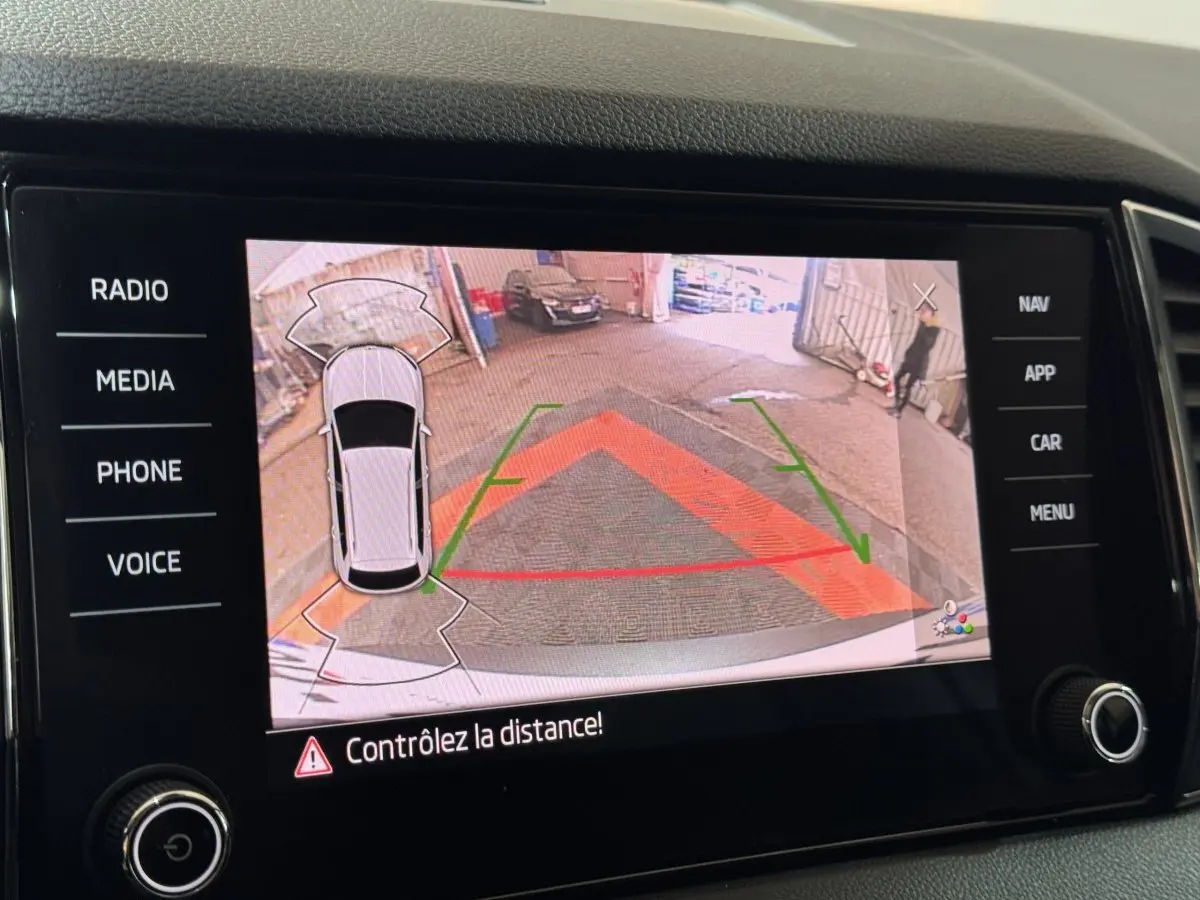 Écran tactile affichant la caméra de recul du Skoda Karoq blanc, avec repères de stationnement colorés.