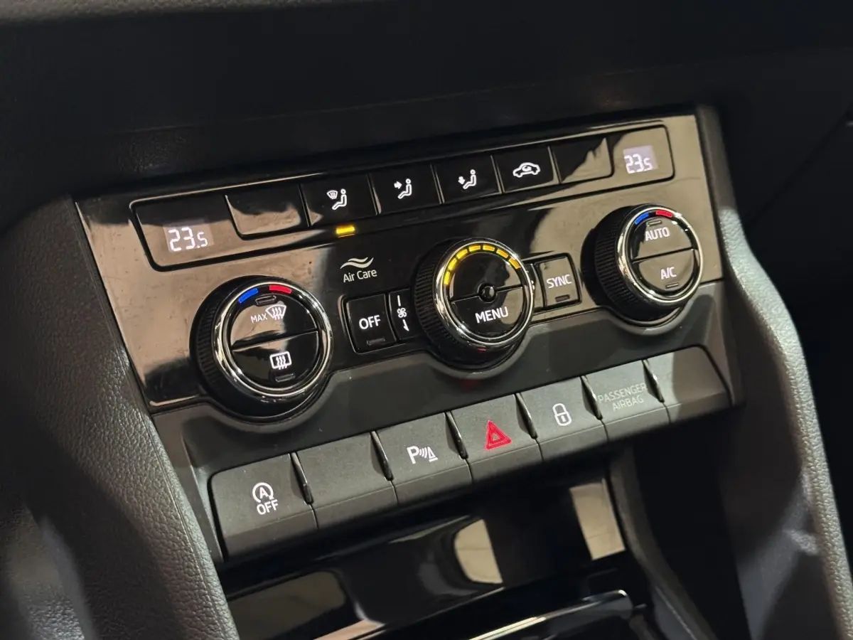 Gros plan sur la console centrale noire du SKODA KAROQ blanc 2021, montrant les commandes de climatisation digitale et boutons fonctionnels.