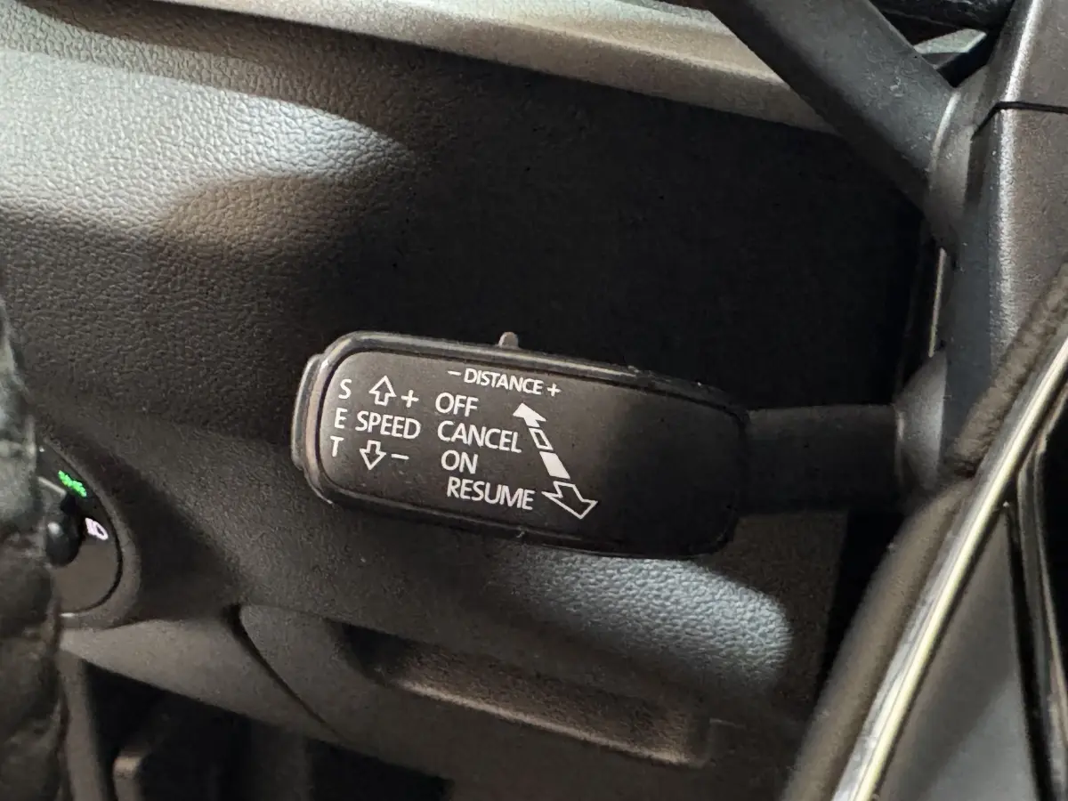 Gros plan sur la commande de régulateur de vitesse au volant d’un Skoda Karoq blanc, intérieur noir.