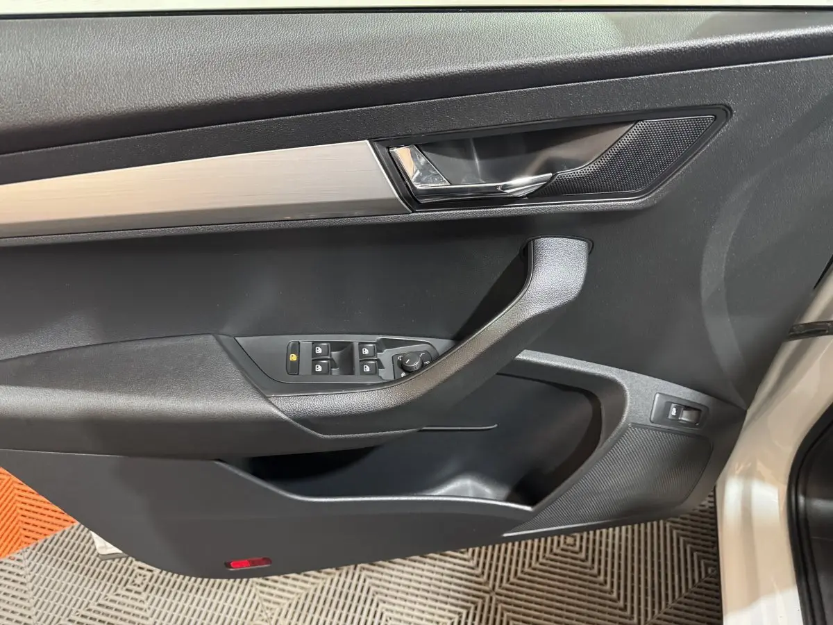 Vue intérieure du panneau de porte côté conducteur du Skoda Karoq blanc, avec commandes électriques et poignée noire.