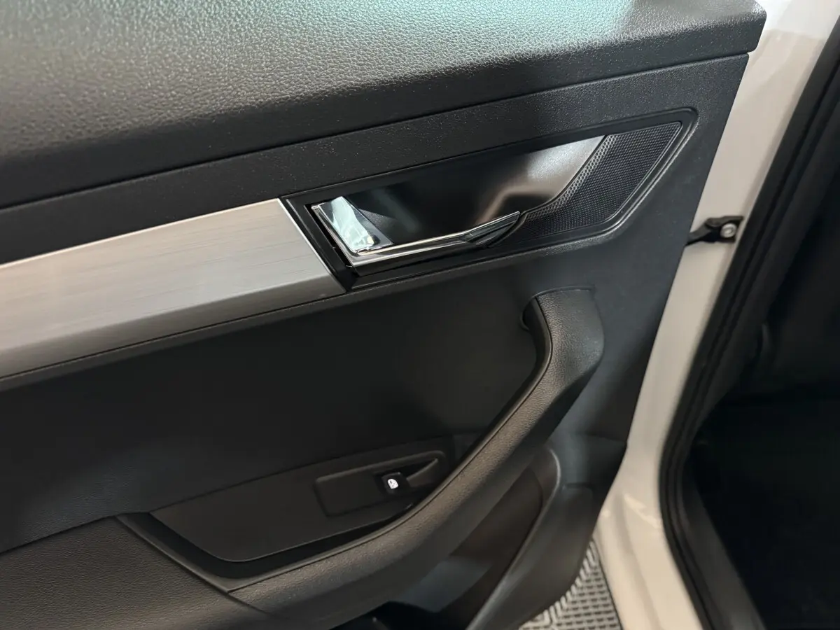 Poignée intérieure côté gauche de la porte avant d'une Skoda Karoq blanche avec insert argenté et bouton de verrouillage.