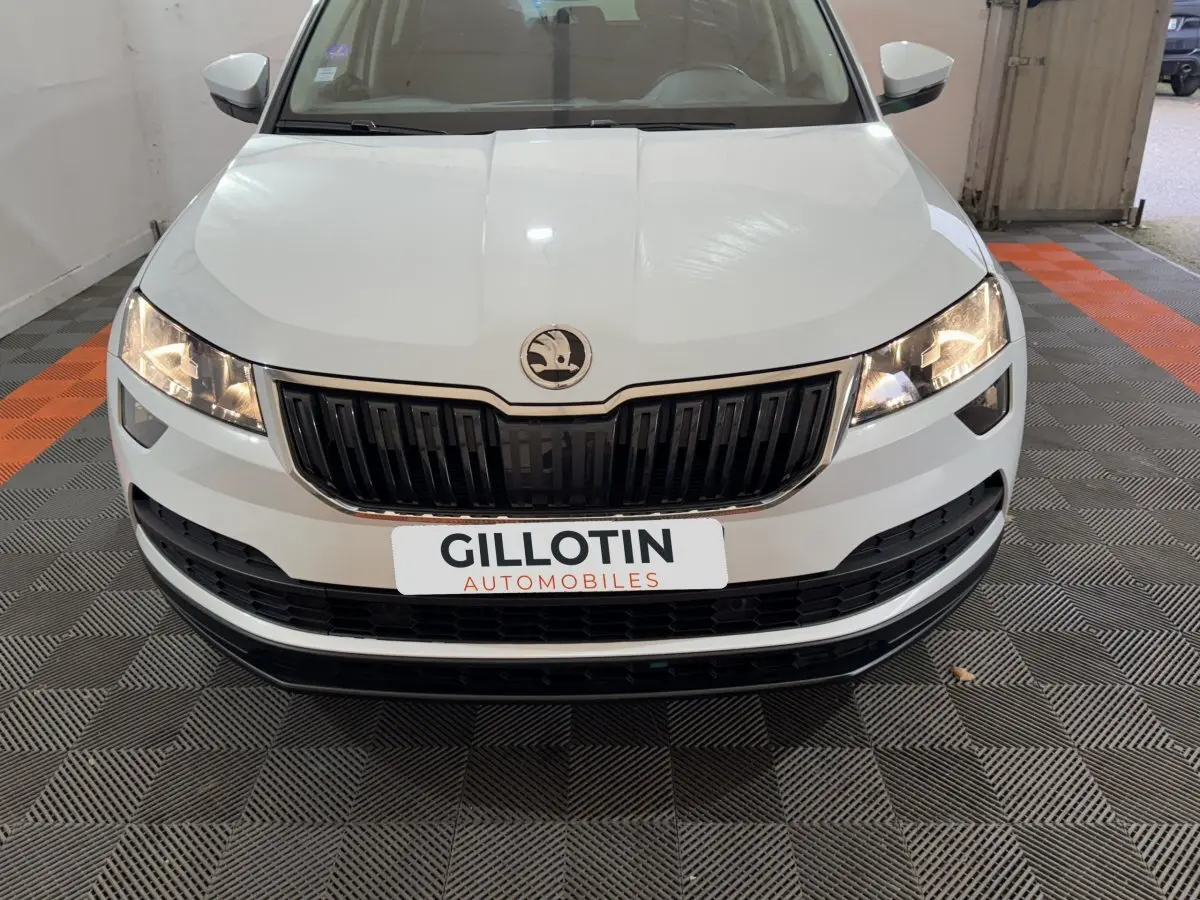 Vue frontale d'un Skoda Karoq blanc avec calandre noire et phares allumés dans un garage.