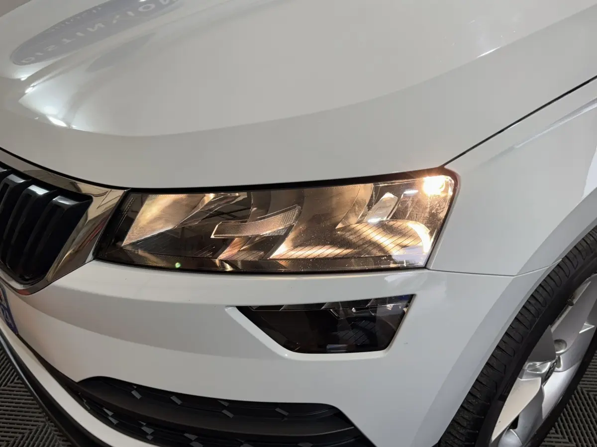 Gros plan sur le phare avant droit allumé d’un Skoda Karoq blanc avec calandre et jante visibles.