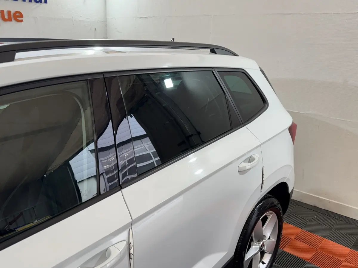 Vue côté droit arrière d'un Skoda Karoq blanc 2021 avec jantes alliage et barres de toit noires.